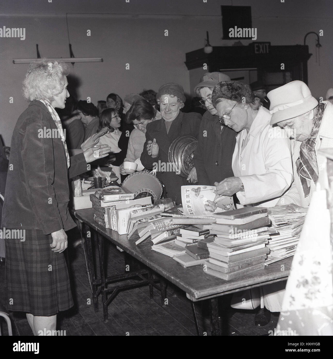 1960s, historical, ladies looking through the comics, books and general bric-a-brac for sale on a taple-top stall at an indoor jumble sale, England. Stock Photo