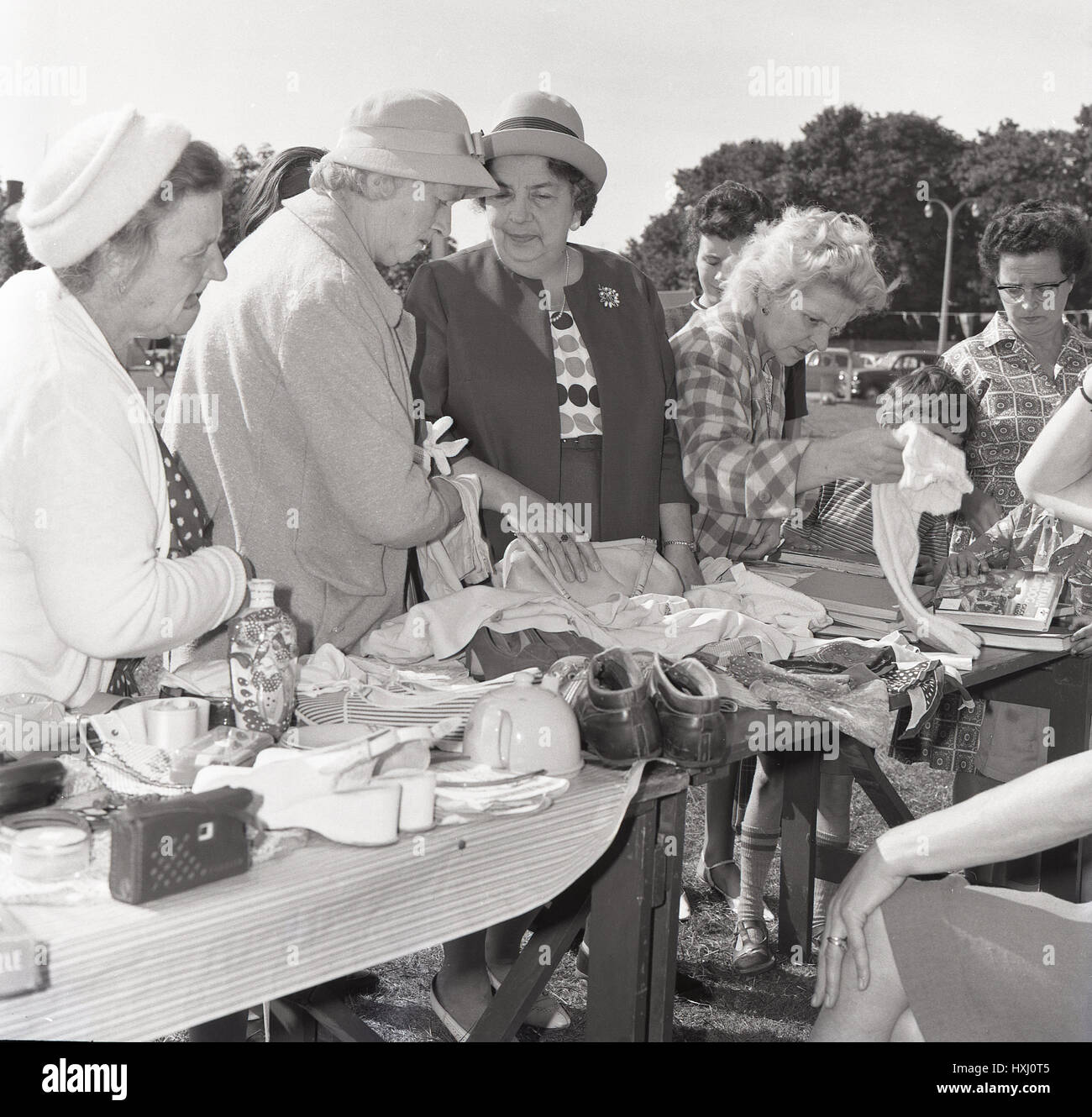 1960s, ladies looking through the various second-hand goods or bric-a-brac available on a stall at an outside jumble sale, England. Stock Photo