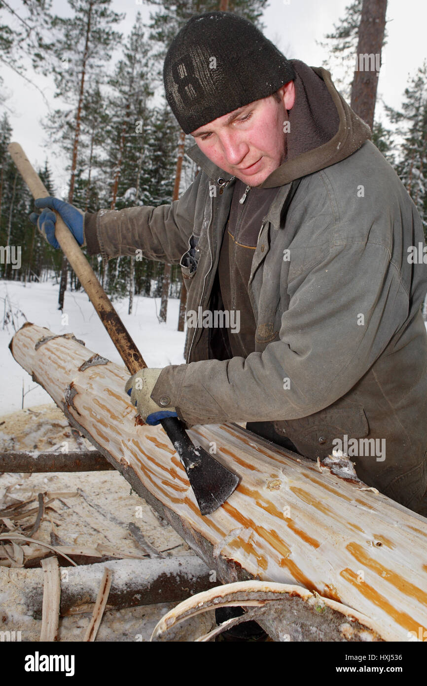 Leningrad Region, Russia - February 2, 2010: The process of peeling and debarking of wood, hand peeling logs with a drawknife. Stock Photo
