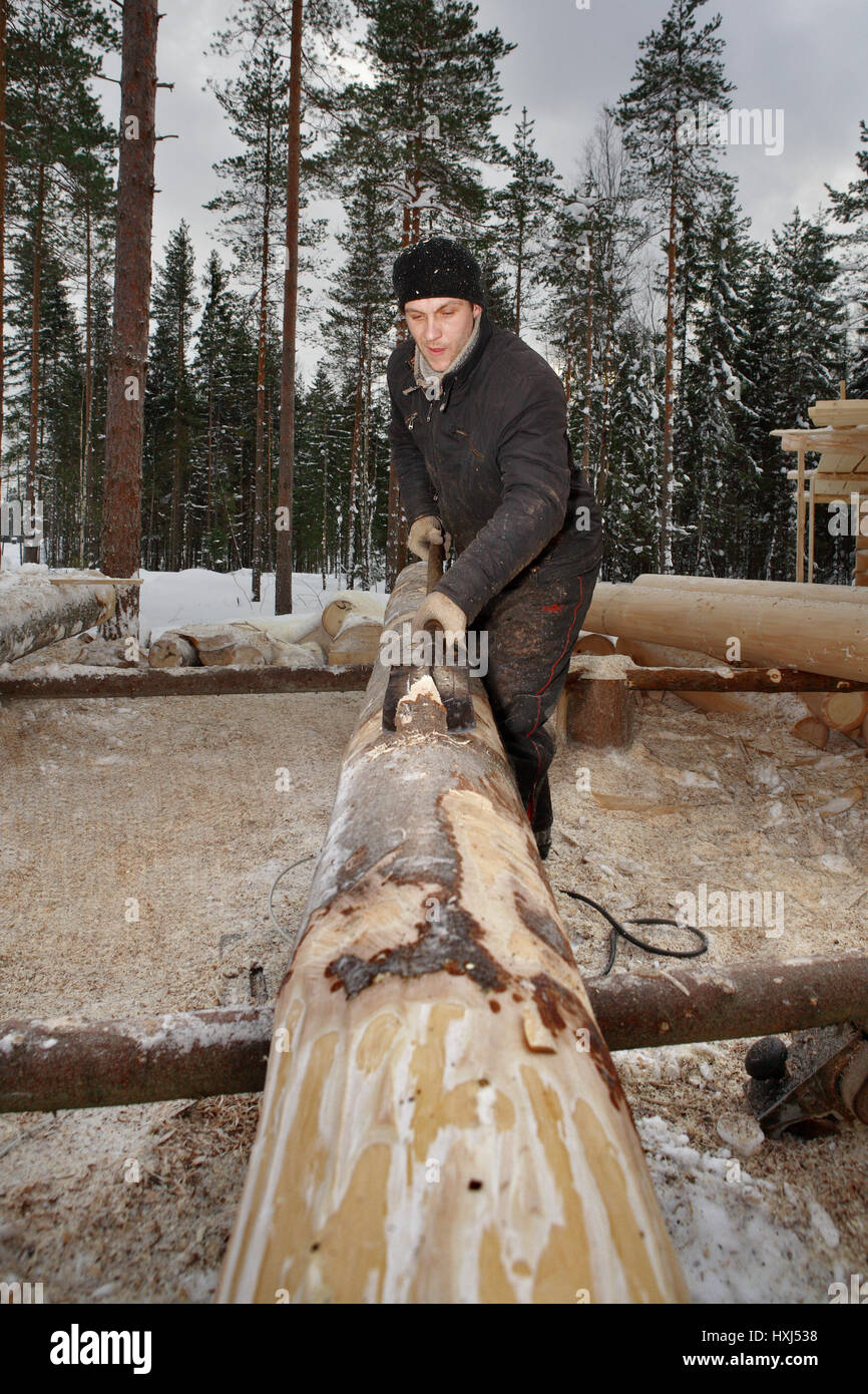 Leningrad Region, Russia - February 2, 2010: The process of peeling and debarking of wood, Worker the logs are hand peeled using a drawknife. Stock Photo