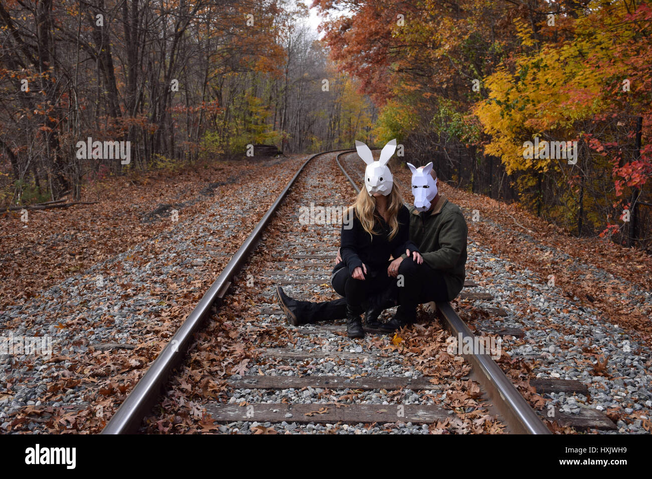 man and woman sitting in train tracks wearing a white horse and white rabbit mask Stock Photo