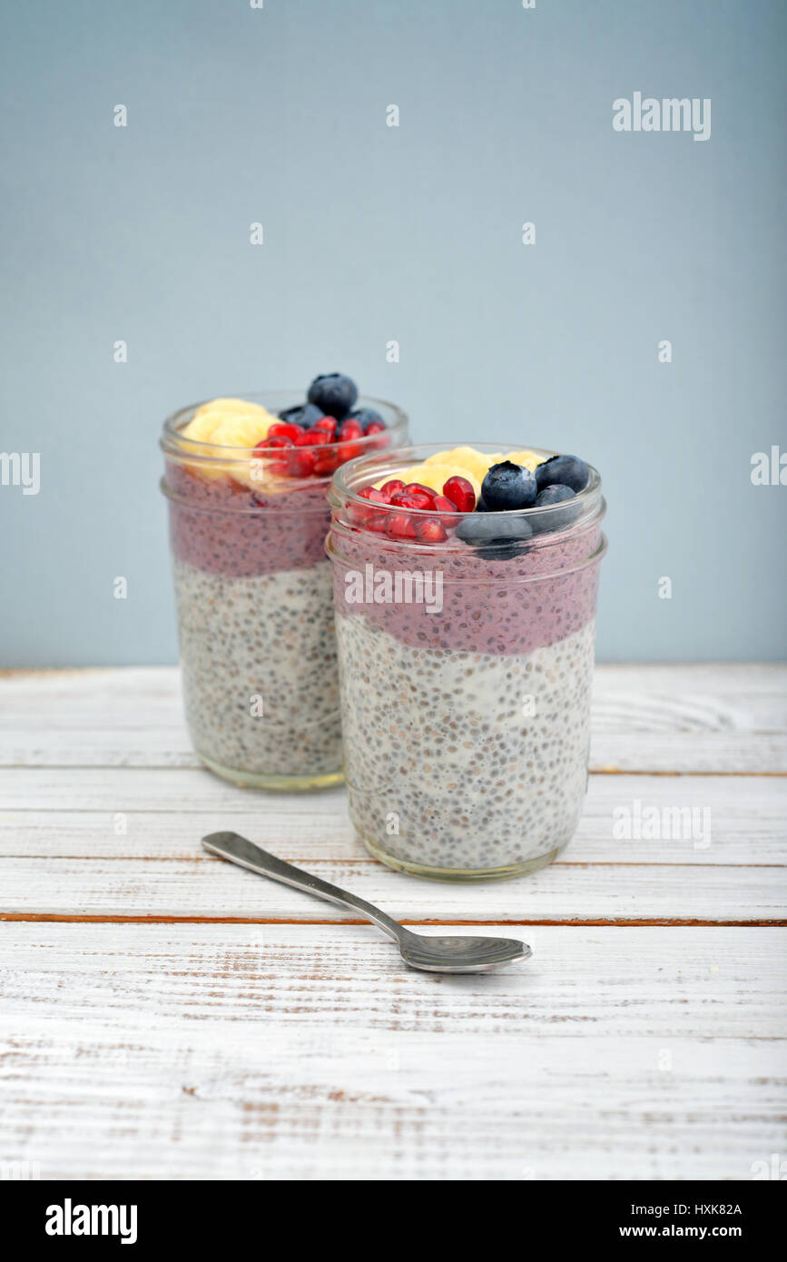 Pudding with chia seeds, yogurt and fresh fruits in glass jars on blue background Stock Photo
