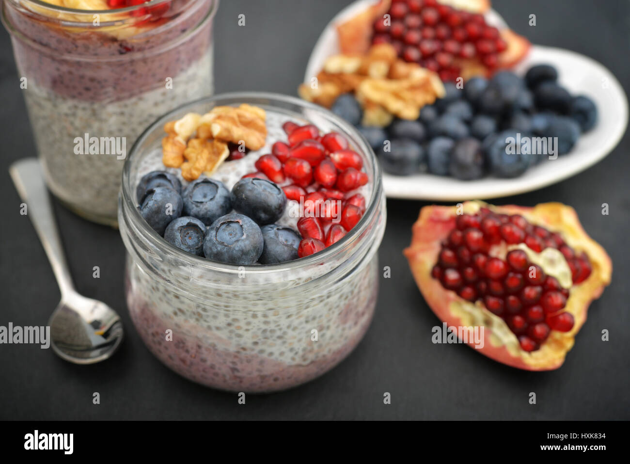 Pudding with chia seeds, yogurt and fresh fruits in glass jars on black background Stock Photo