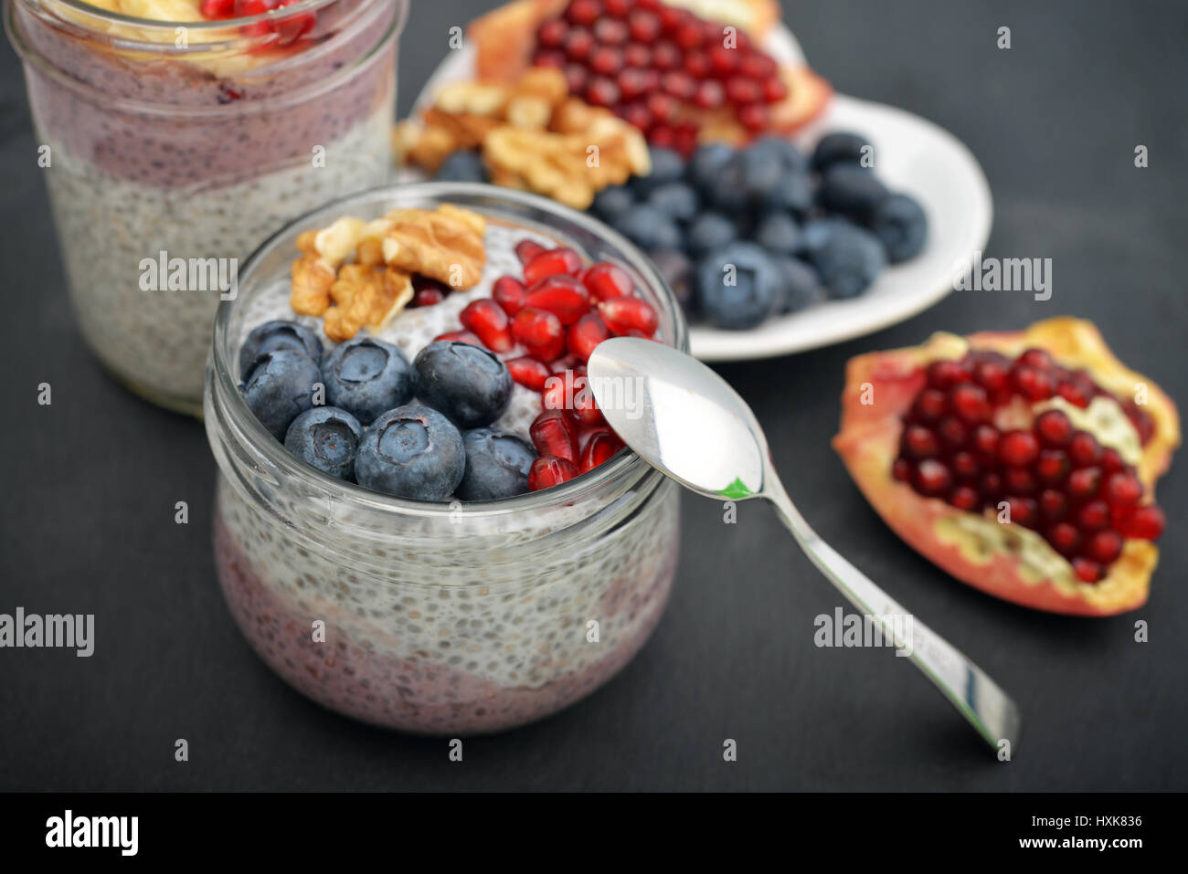 Pudding with chia seeds, yogurt and fresh fruits in glass jars on black background Stock Photo