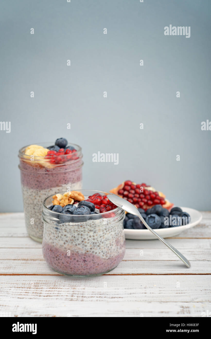 Pudding with chia seeds, yogurt and fresh fruits in glass jars on blue background Stock Photo
