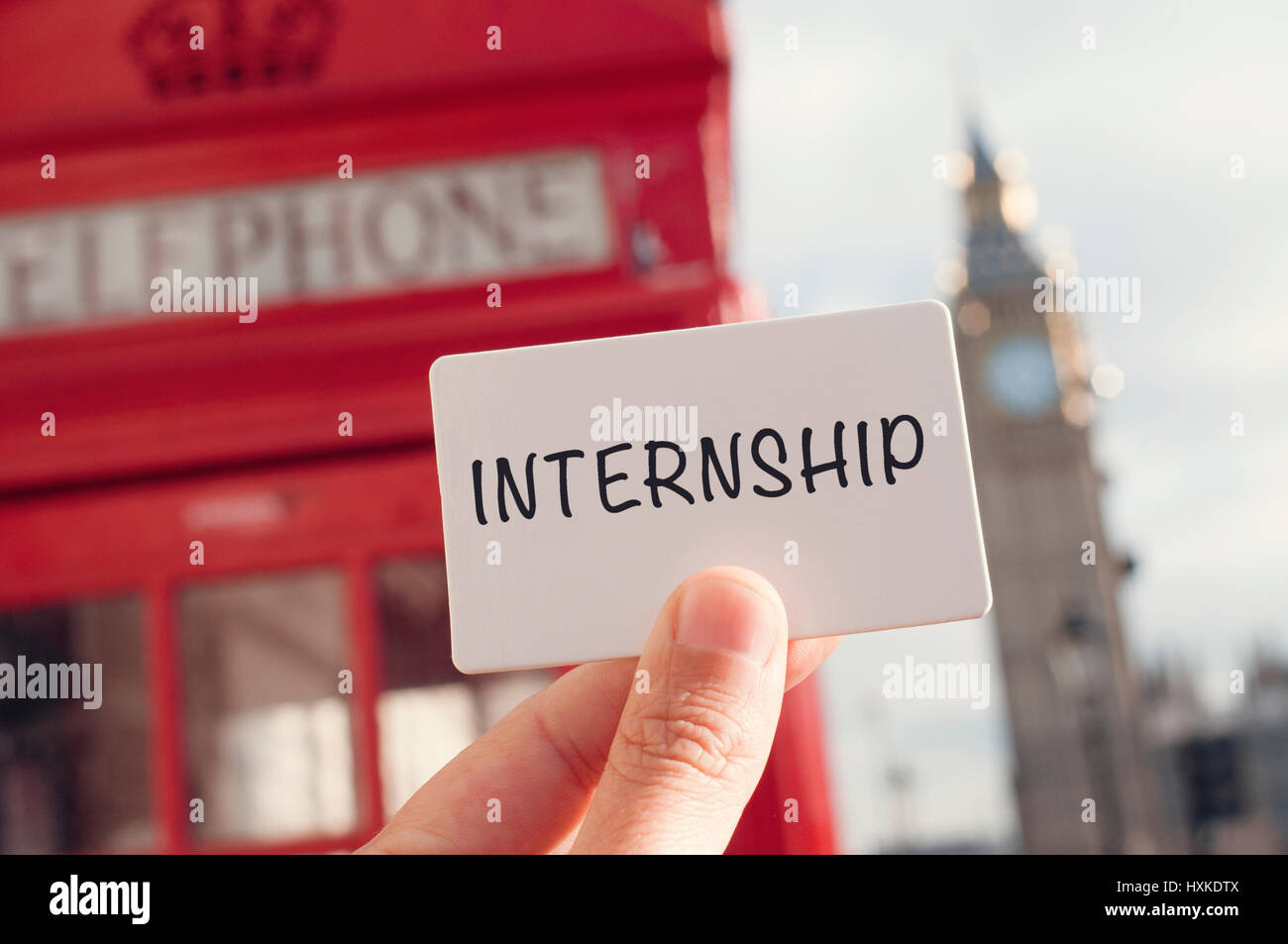 the hand of a young man showing a signboard with the word internship with a red telephone booth and the Big Ben in the background, in London, United K Stock Photo