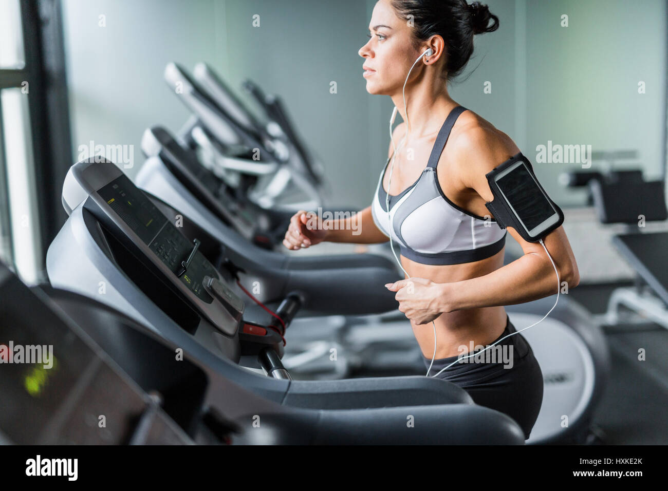 Sportive Woman Running on Treadmill with Music Stock Photo