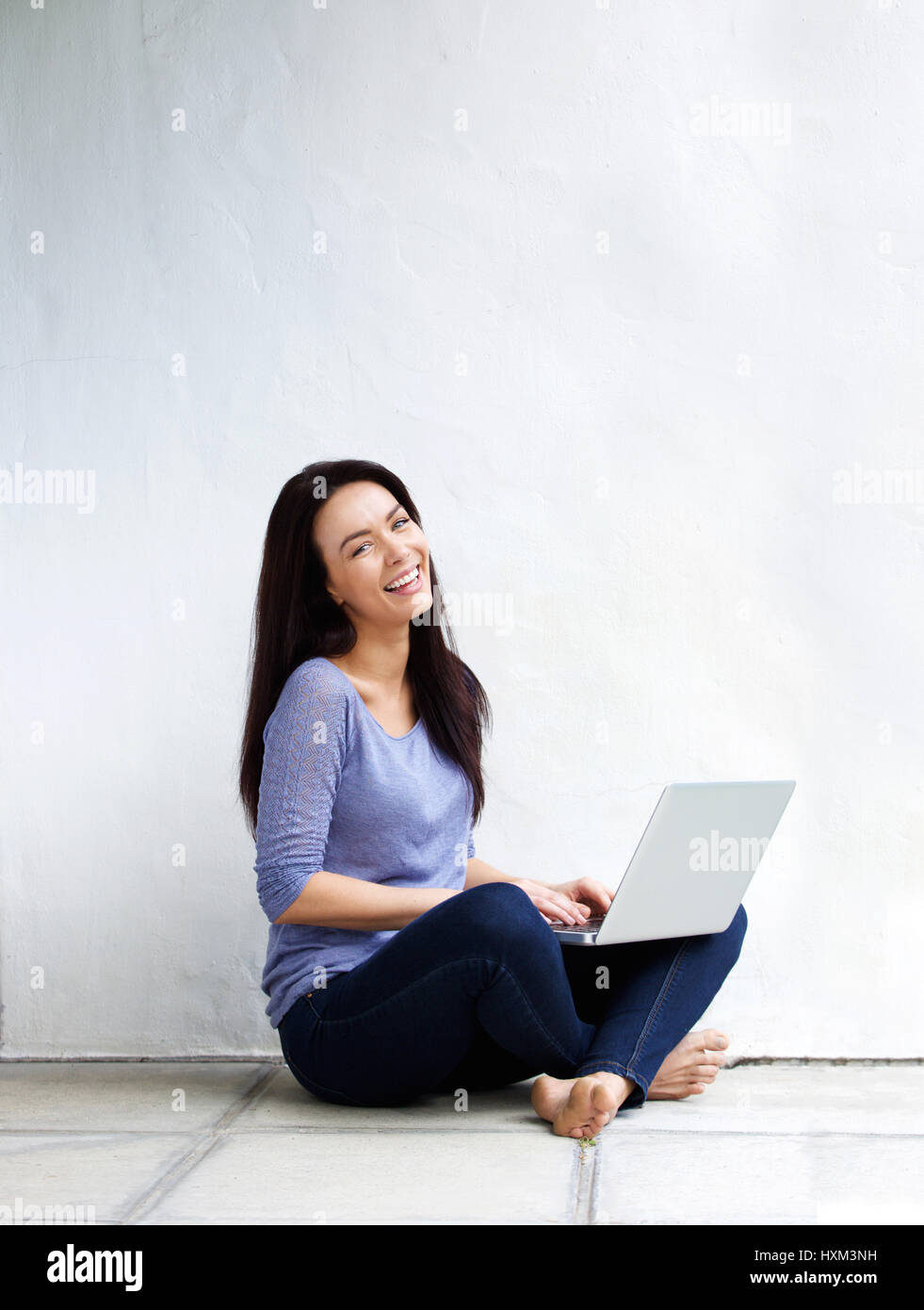 Portrait of happy young woman sitting on floor at home with a laptop ...