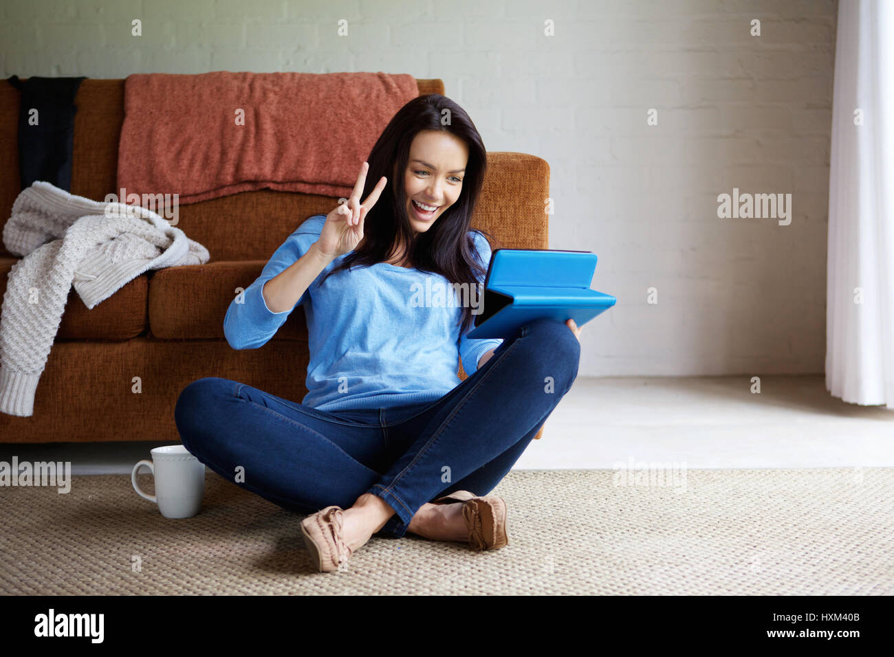 Portrait of smiling young woman sitting on floor in living room with ...