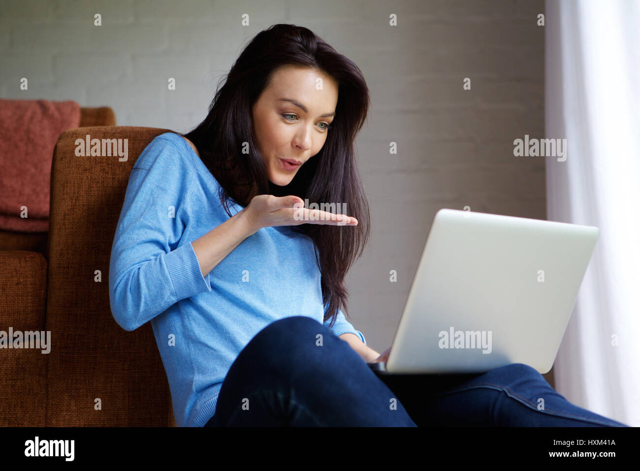 Portrait of happy young woman blowing a kiss at laptop during a video chat Stock Photo