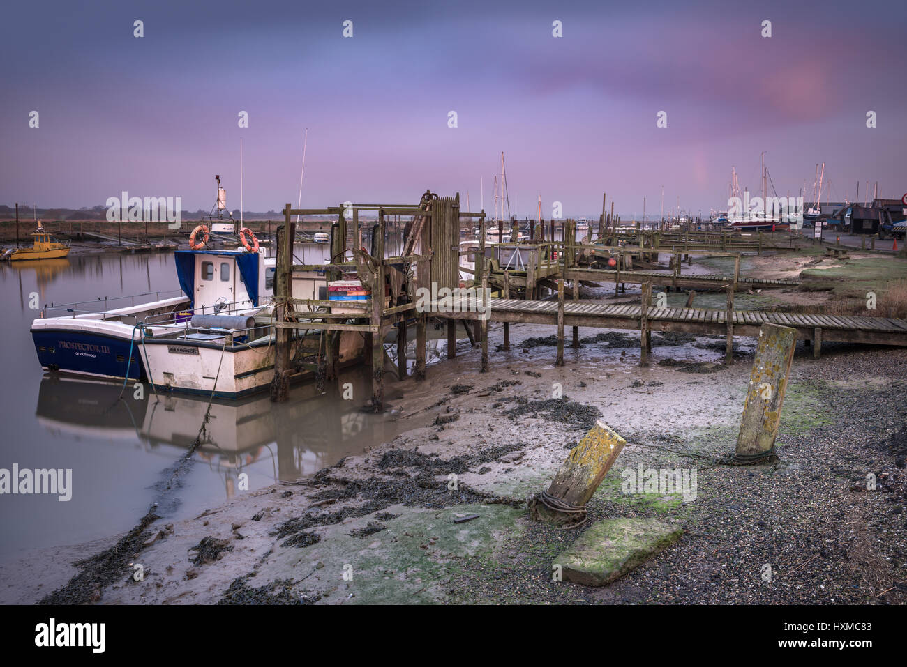 The remnants of a rainbow fade over the fishing boats moored to the pontoons on Blackshore in Southwold, Suffolk, at dawn in mid March. Stock Photo