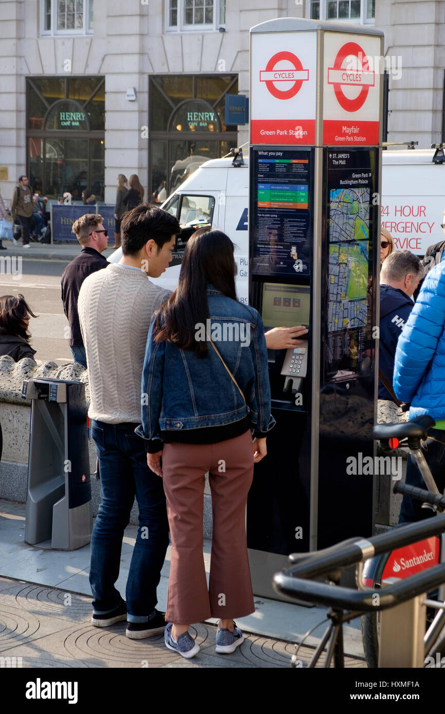 Two asian tourists using a machine to hire a bike outside Green Park tube station in London Stock Photo