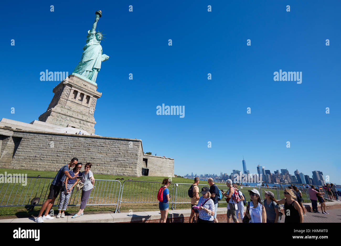Tourists shooting selfies and walking near Statue of Liberty in a sunny day, clear blue sky in New York Stock Photo