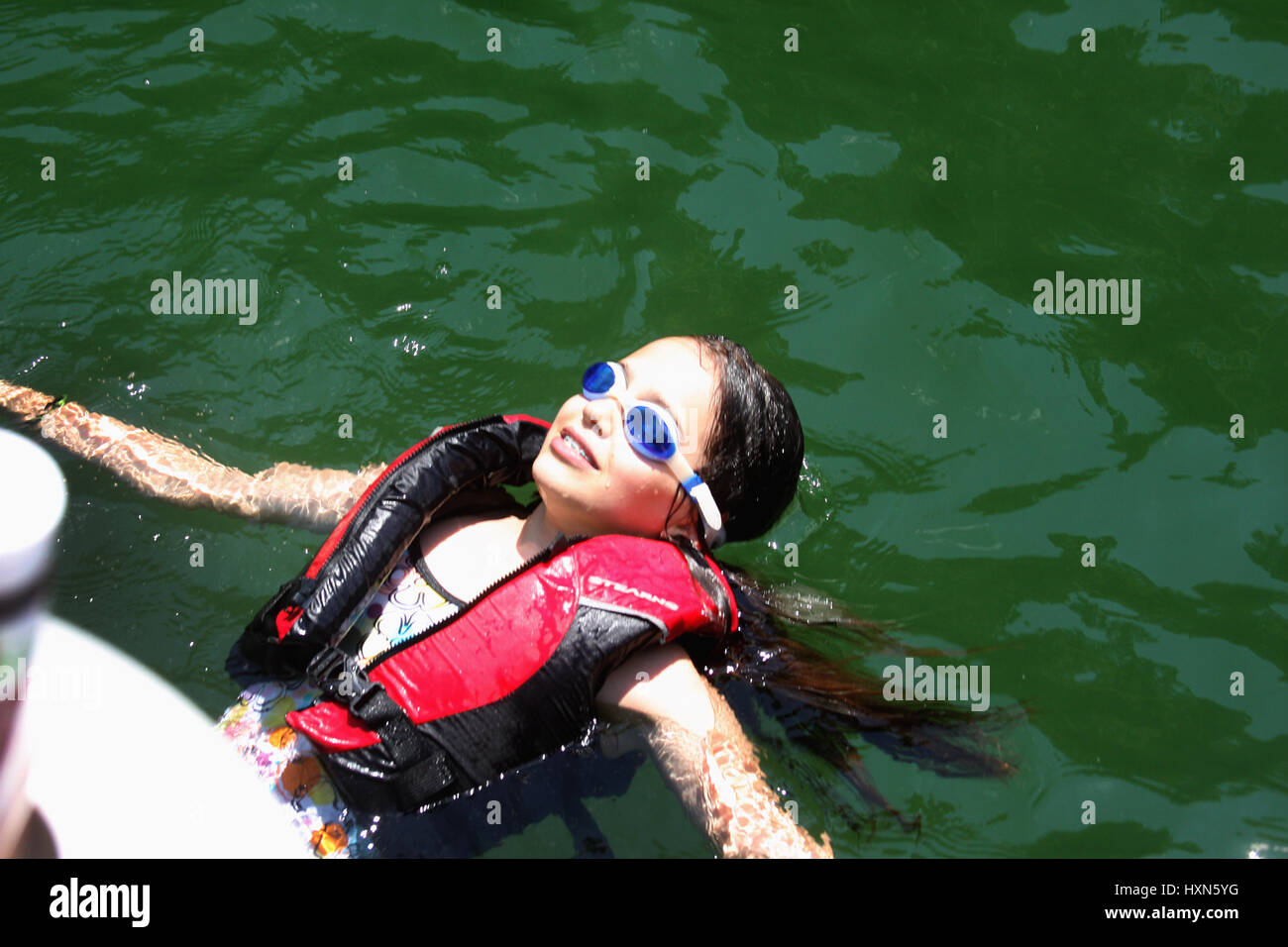 Young girl floating in water with safety vest and goggles Stock Photo