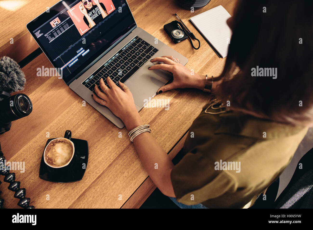High angle view of female vlogger editing video on laptop. Young woman working on computer with coffee and cameras on table. Stock Photo