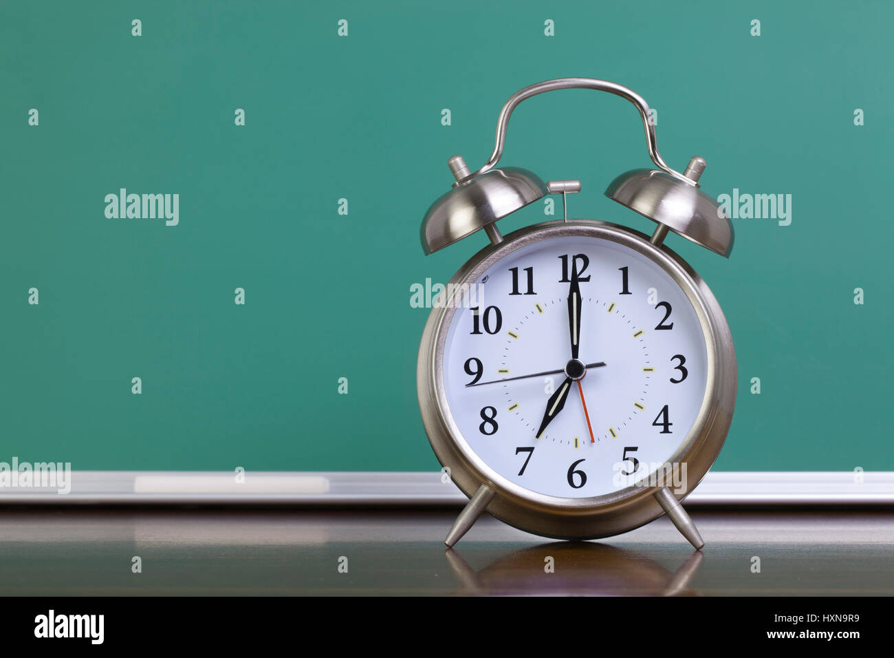 A silver alarm clock in front of a green chalkboard Stock Photo