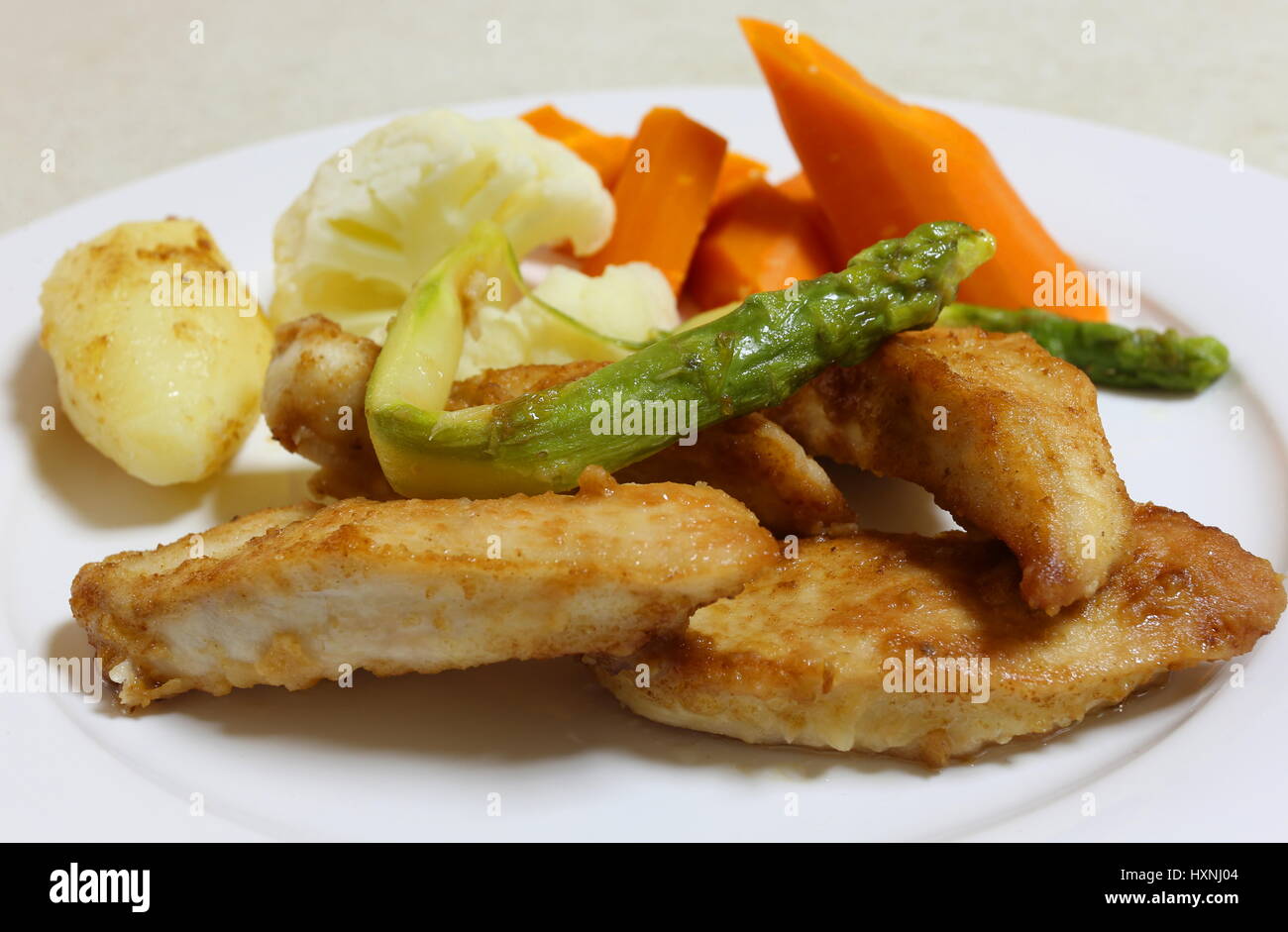 Pan fried chicken, coated with seasoned flour and served with asparagus and steamed vegetables Stock Photo