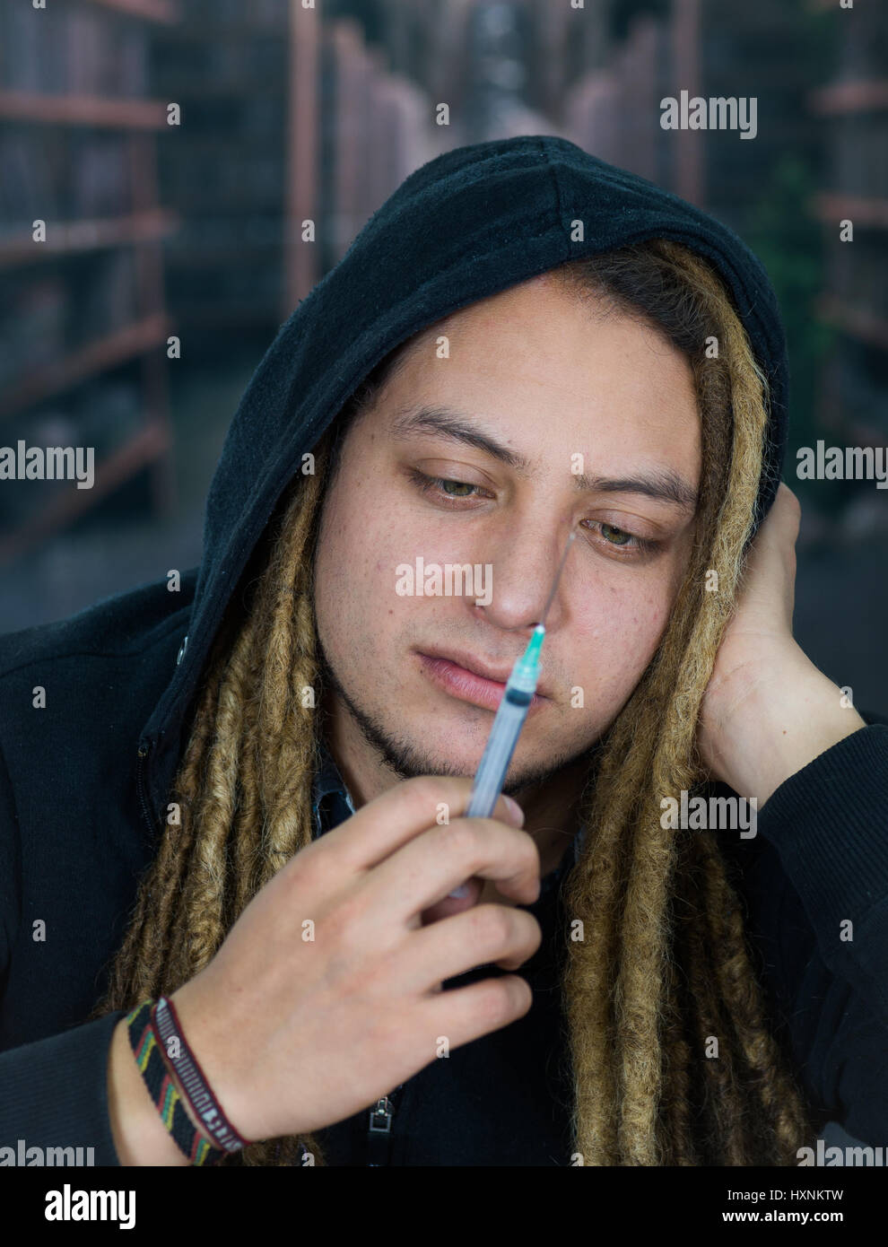 Man holding up syringe to camera with dopey facial expression, resting head on hand, drug addiction concept Stock Photo