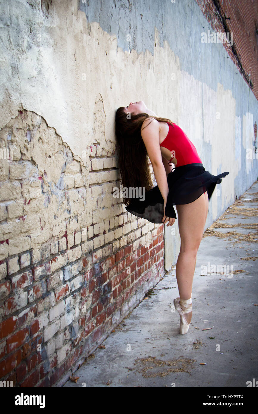 Young brunette ballerina up on point leaning dramatically against an rustic brick wall Stock Photo