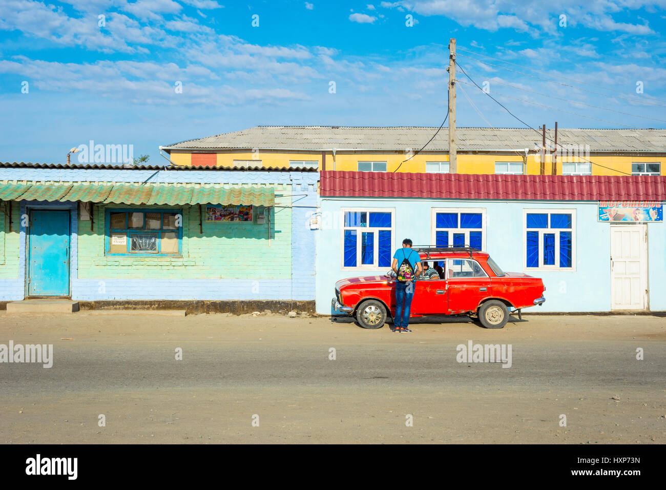 Two men talking at red lada car. Muynak, Uzbekistan Stock Photo