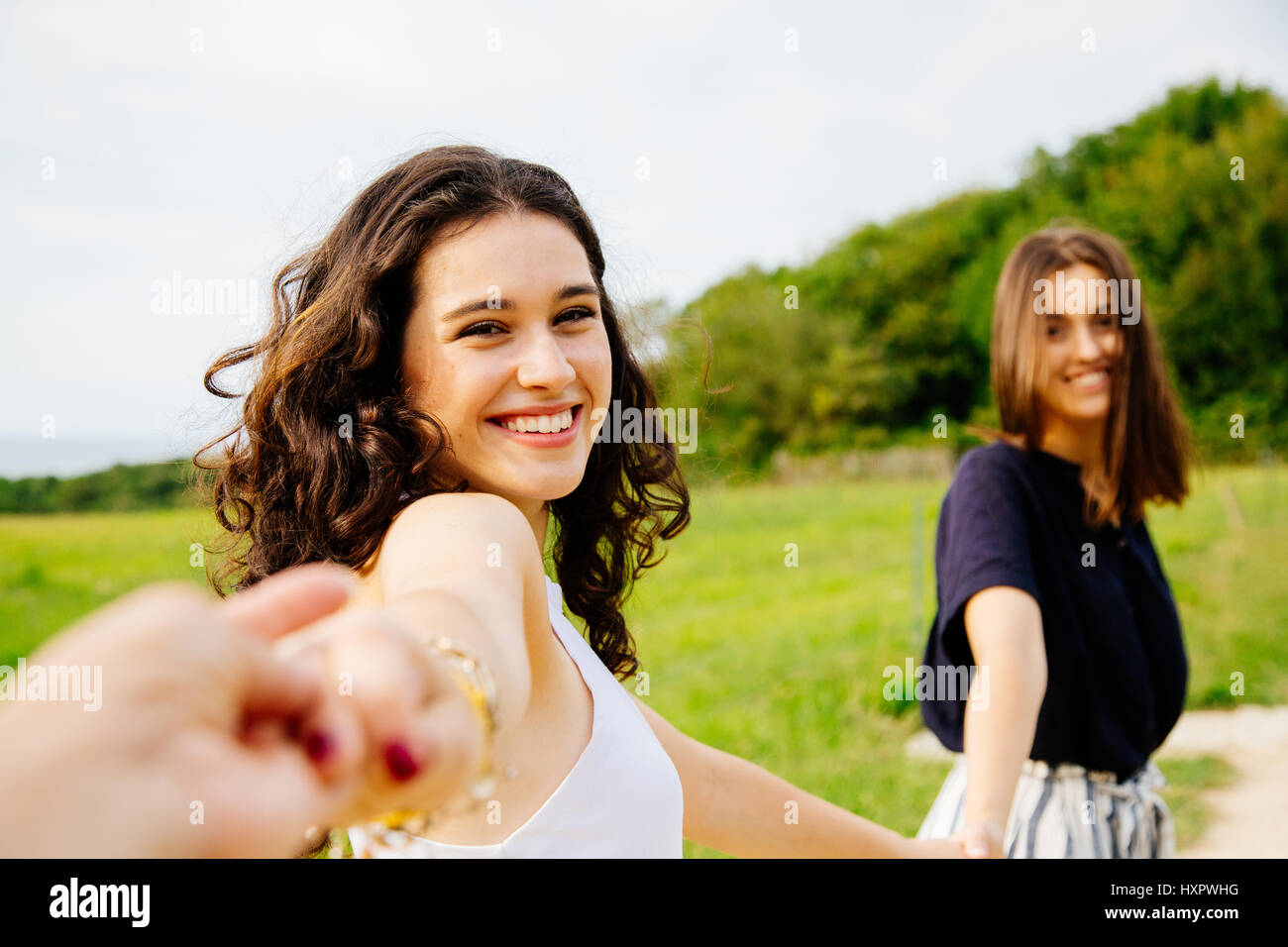 Two happy girls running in nature holding hands and turning head to us ...