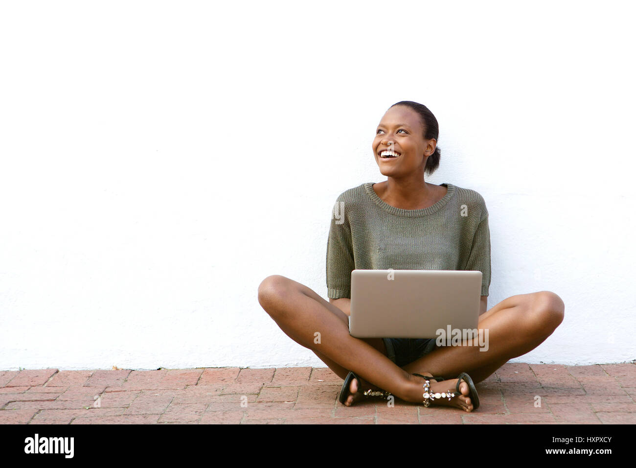 Portrait of happy young african american woman sitting on sidewalk with ...