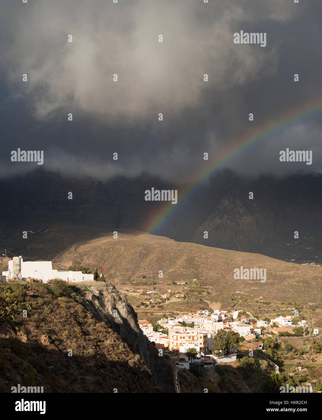 Rainbow over the mountain village of San Bartolome de Tirajana, Gran Canaria, apparently ending at the cross of village church, from Mirador de Tunte Stock Photo