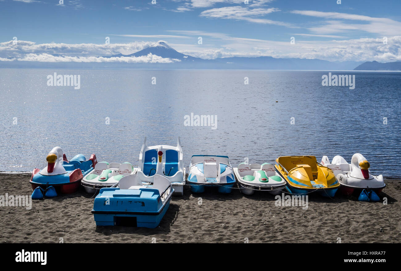 Fun boats for rent on the  beach, lake lago llanquihue, volcano Osorno covered by clouds, village Frutilliar,  chilenean lake district, Chile Stock Photo
