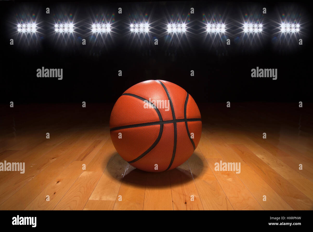 A basketball on a wood floor beneath bright arena lights Stock Photo