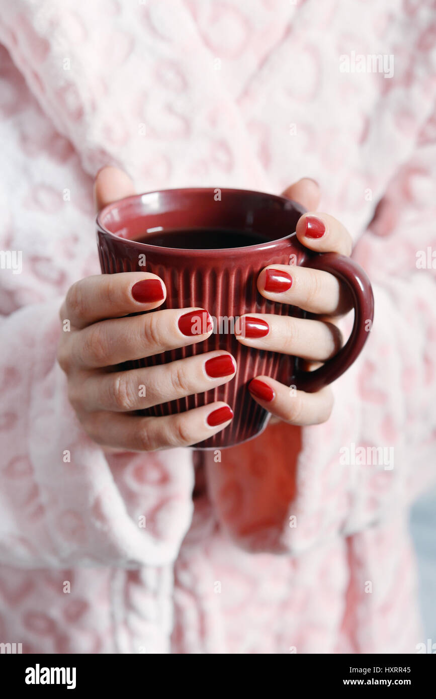 Women in pink bathrobe holds mug with coffee in hands Stock Photo