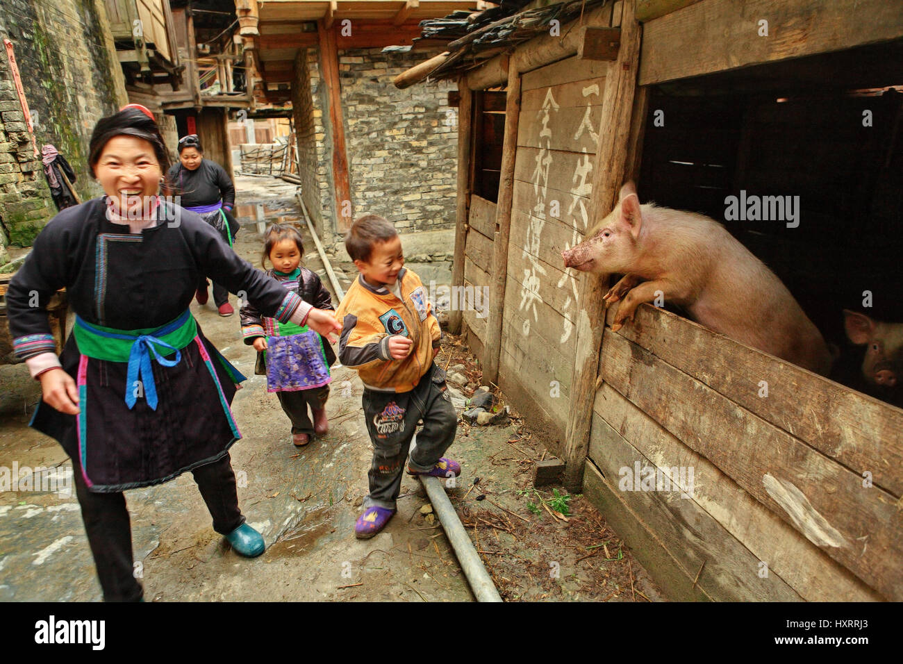 Zengchong village, Guizhou, China - April 13, 2010: The family of Chinese peasants with kids, pass past the pigsty, April 13, 2010. Asian peasant farm Stock Photo