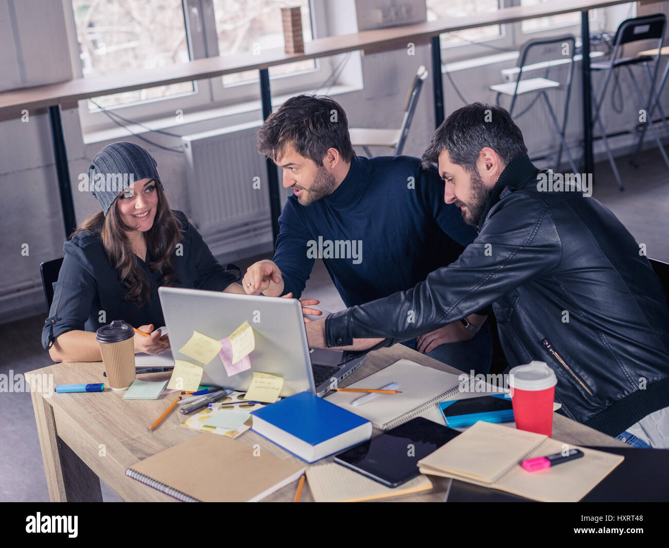 Young smart team. Group of  modern people discussing project on meeting in the office. Working environment with laptop, coffee, notepads and stationer Stock Photo