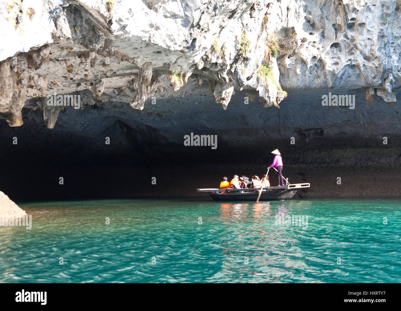 Female rower propels sampan boat into cave on Ha Long Bay Stock Photo