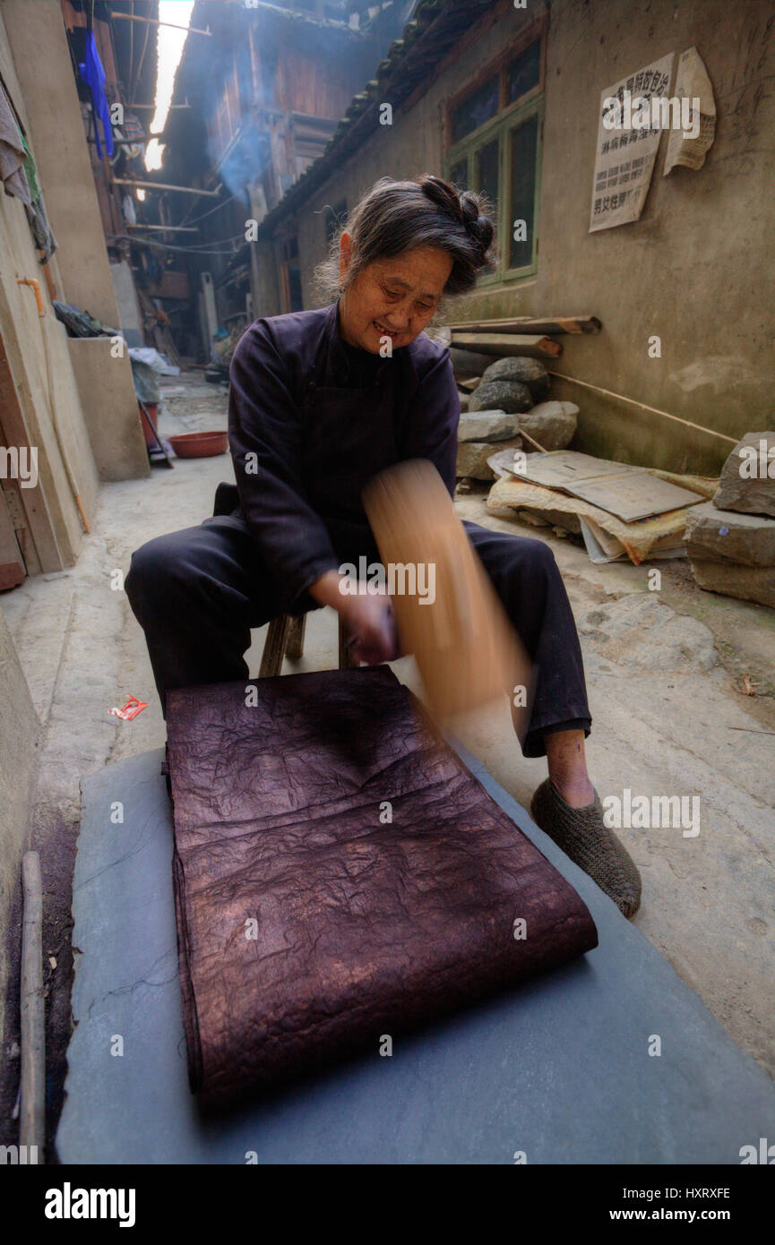 Zhaoxing Dong Village, Guizhou Province, China -  April 9, 2010: Dong woman pounding dyed cotton cloth to make it shiny. Stock Photo