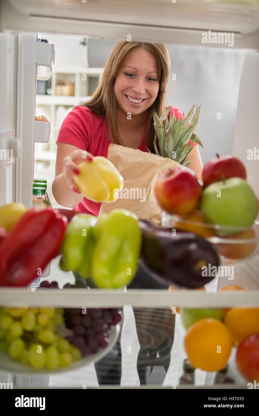 Young housewife put peppers from market in fridge Stock Photo