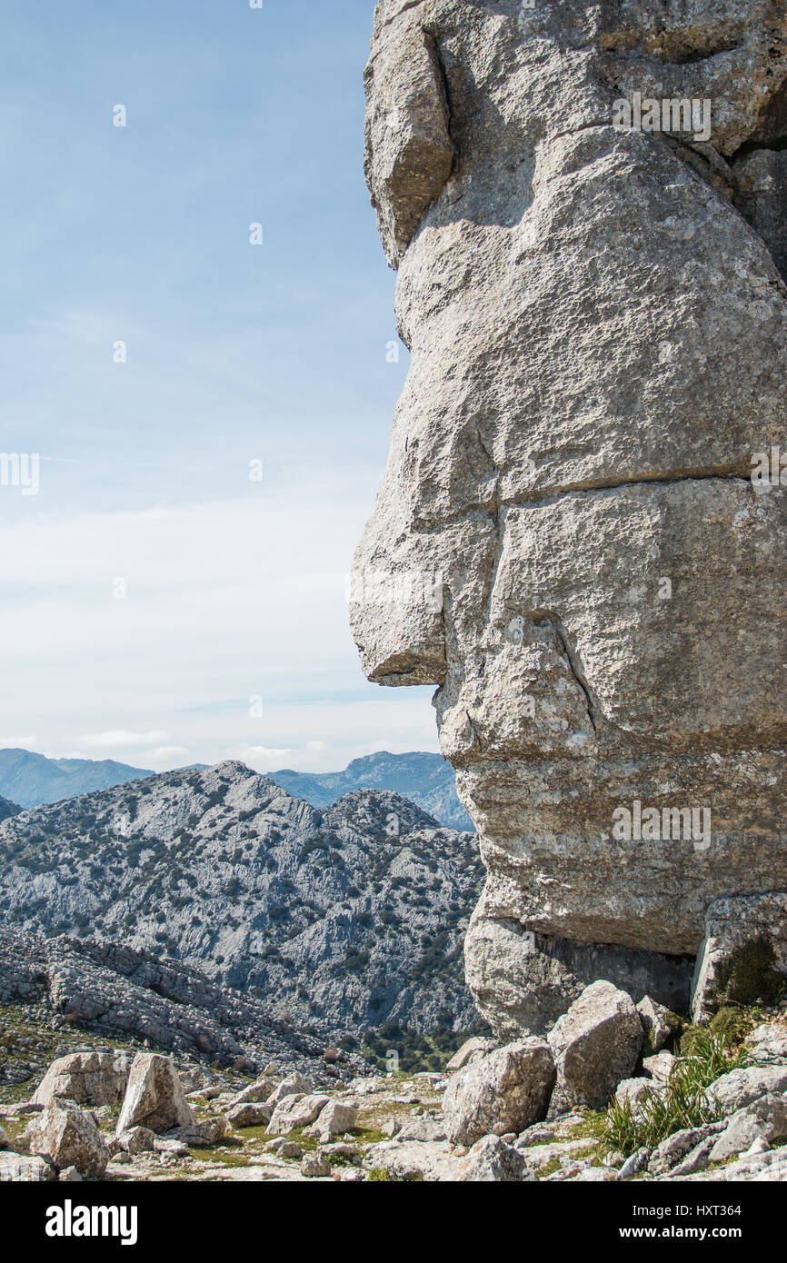 Close-up of red indian side face shape monolith grey rock against of beautiful endless mountain chain Stock Photo