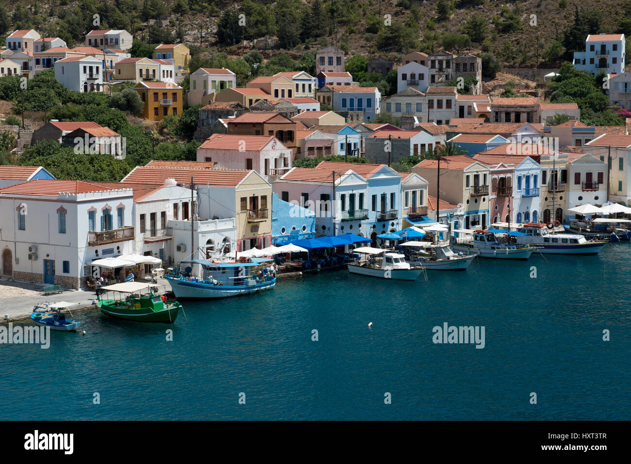 Hafenbecken mit kleinen Booten und einer Reihe von bunten Häusern vor grünem Wasser, Insel Kastellorizo, Dodekanes, Griechenland Stock Photo