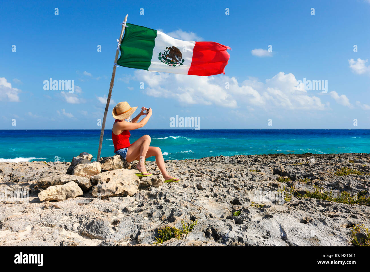 Young woman with a hat taking photo under Mexican flag on Cozumel Stock Photo