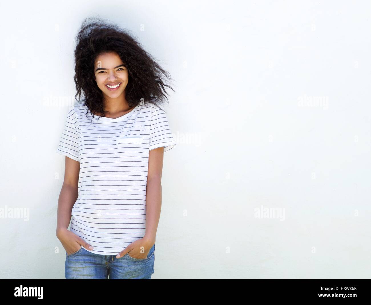 Portrait of a young woman with curly hair smiling against white ...