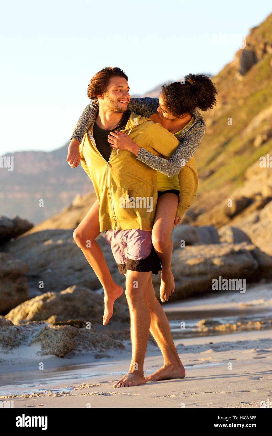 несет на спине. несет девушку на пляже. пареньнесëт девушку на спине. девушка бежит по берегу. катать на спине.