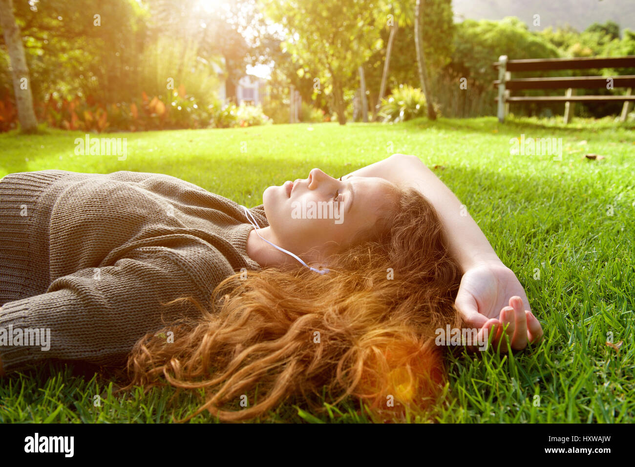 Portrait of an attractive young woman lying on grass listening to music ...