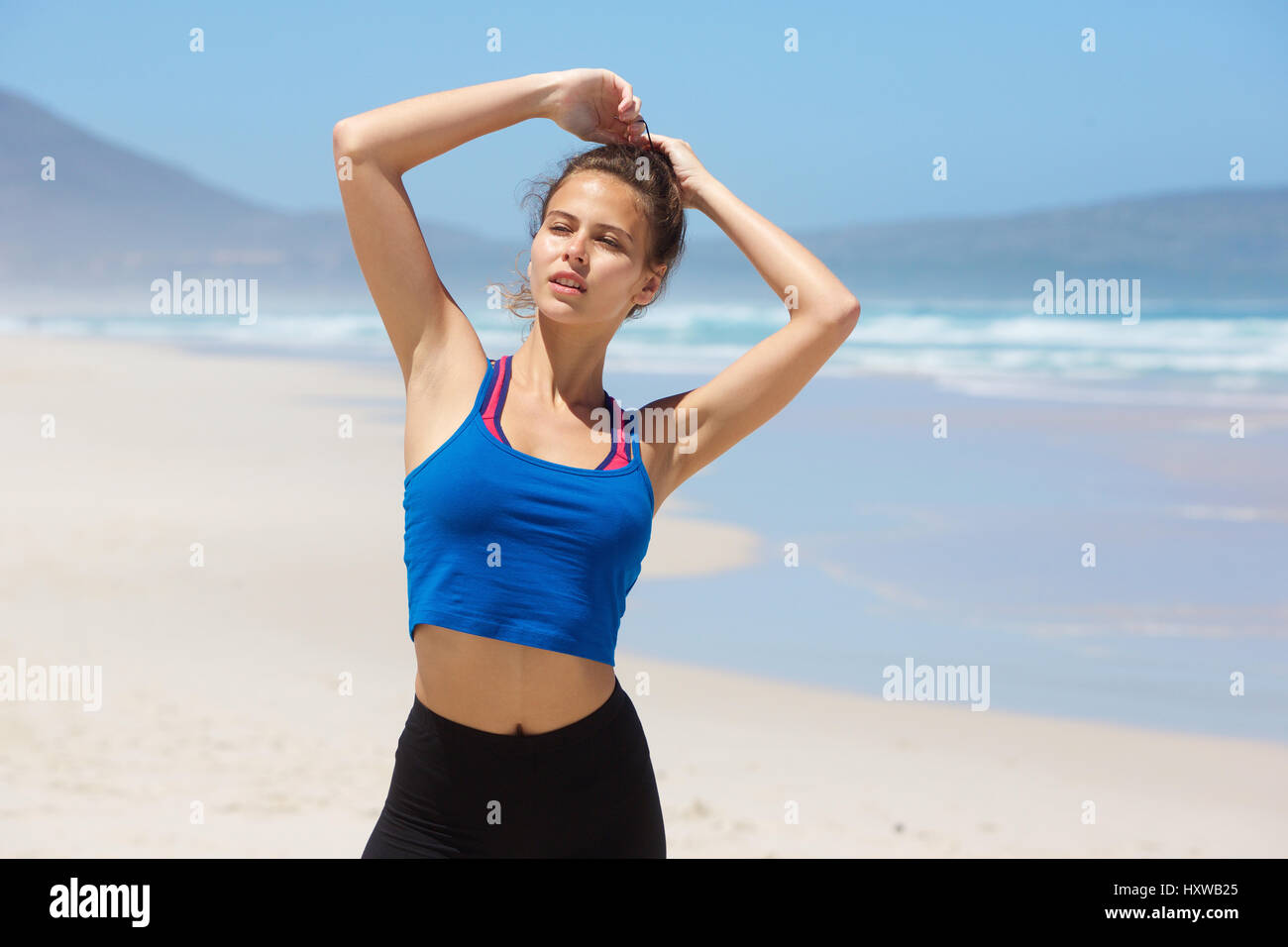 Portrait of a beautiful young woman standing on the beach with hand in ...