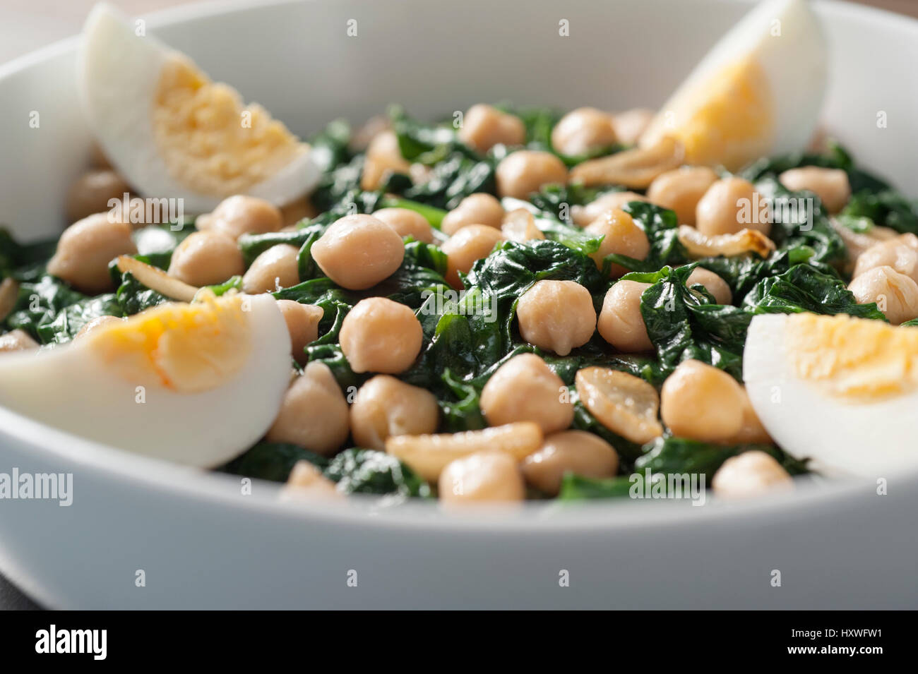boiled spinach salad with chickpeas and hard boiled egg in a white bowl