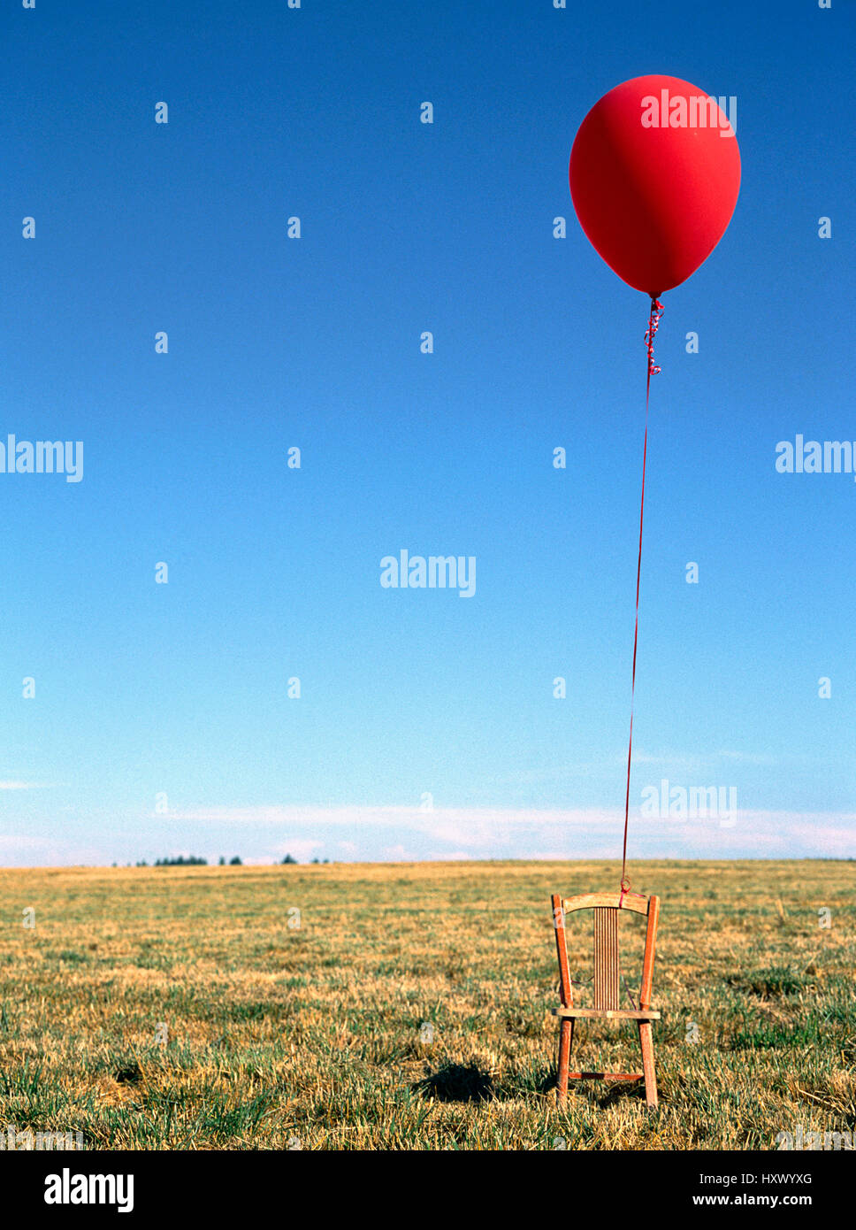 A red balloon tied to and empty child's chair. Stock Photo