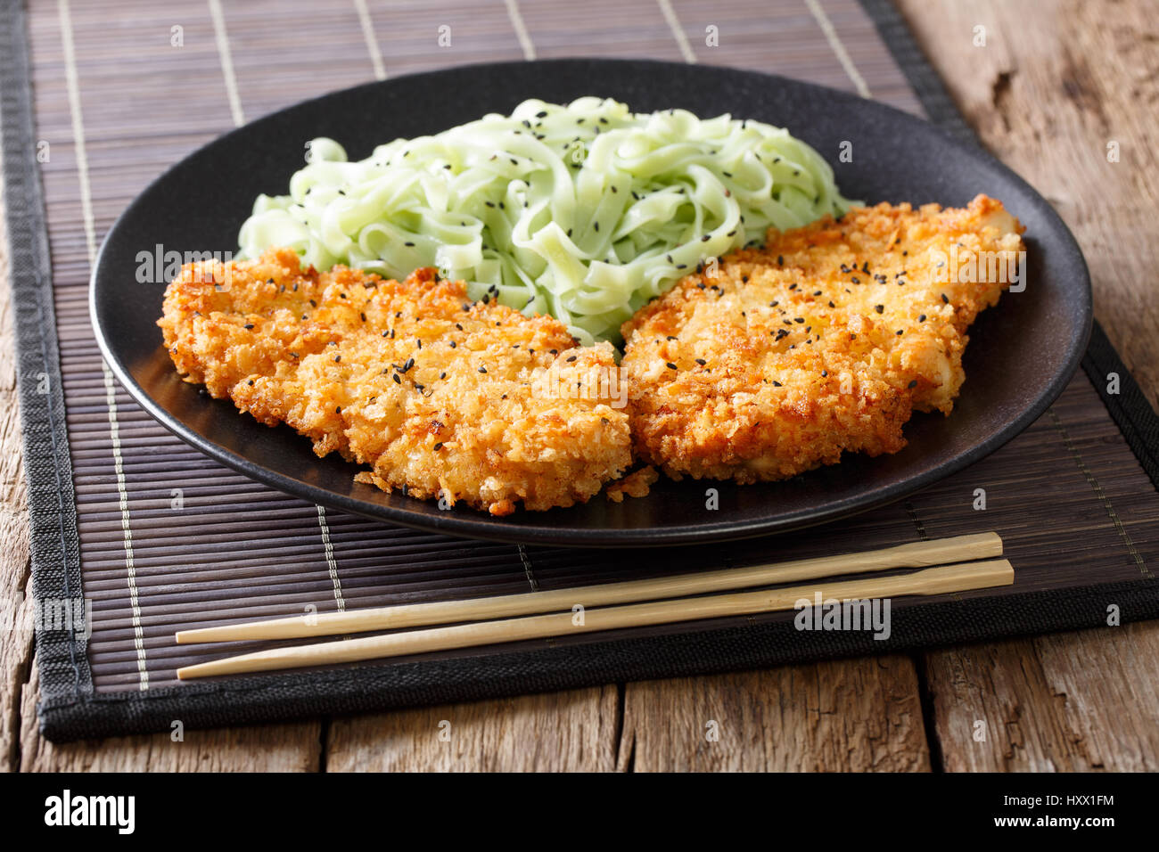 Chicken cutlet in breadcrumbs and green noodles with sesame close-up on the table. horizontal Stock Photo