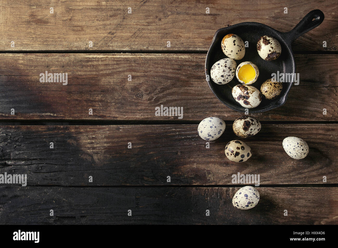 Whole and broken quail eggs with yolk in shell in small iron cast pan