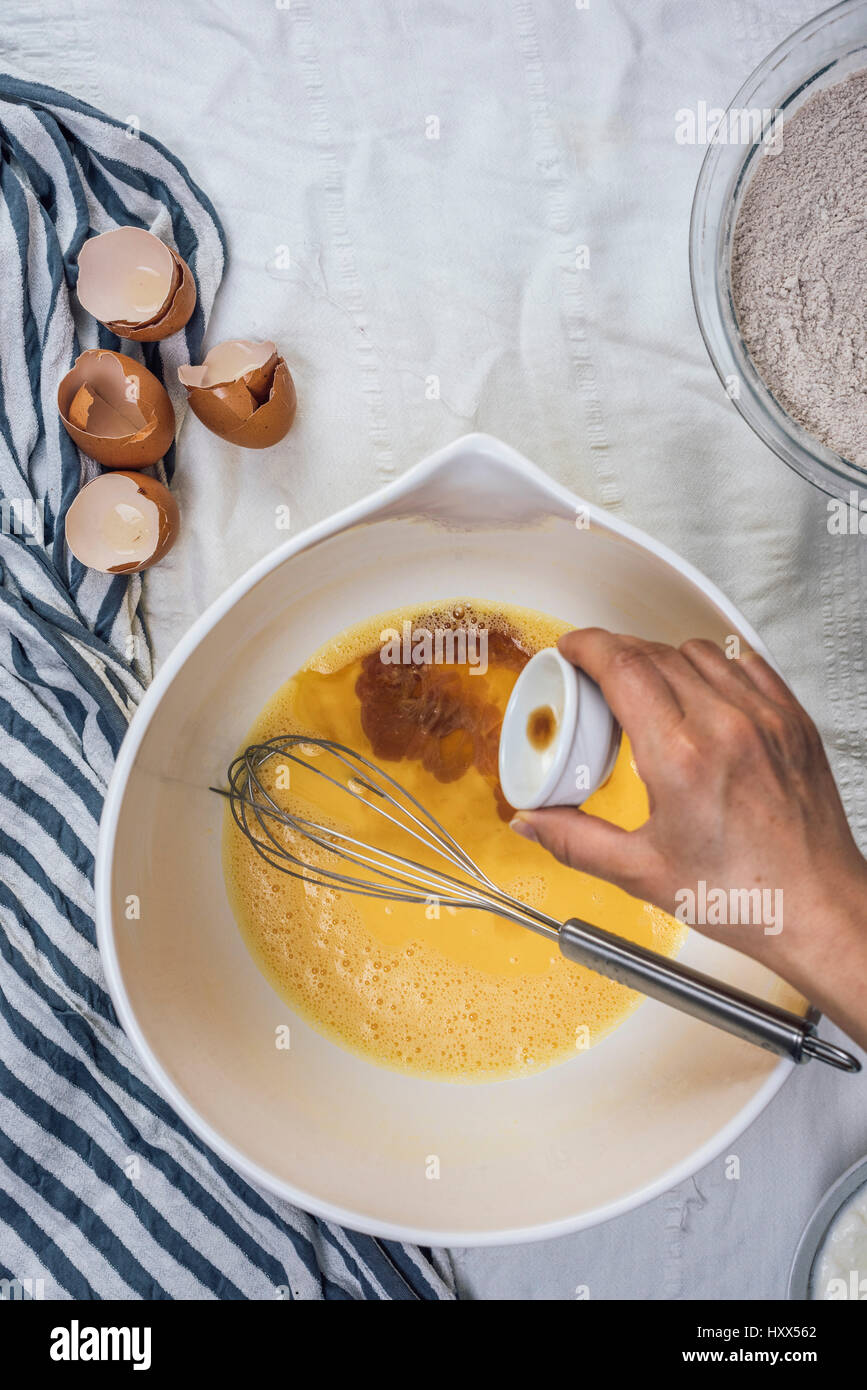 A woman pouring vanilla extract into whisked eggs in a large bowl photographed from top view