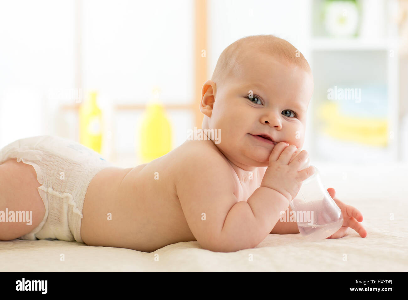 Pretty baby girl drinks water from bottle lying on bed. Child weared