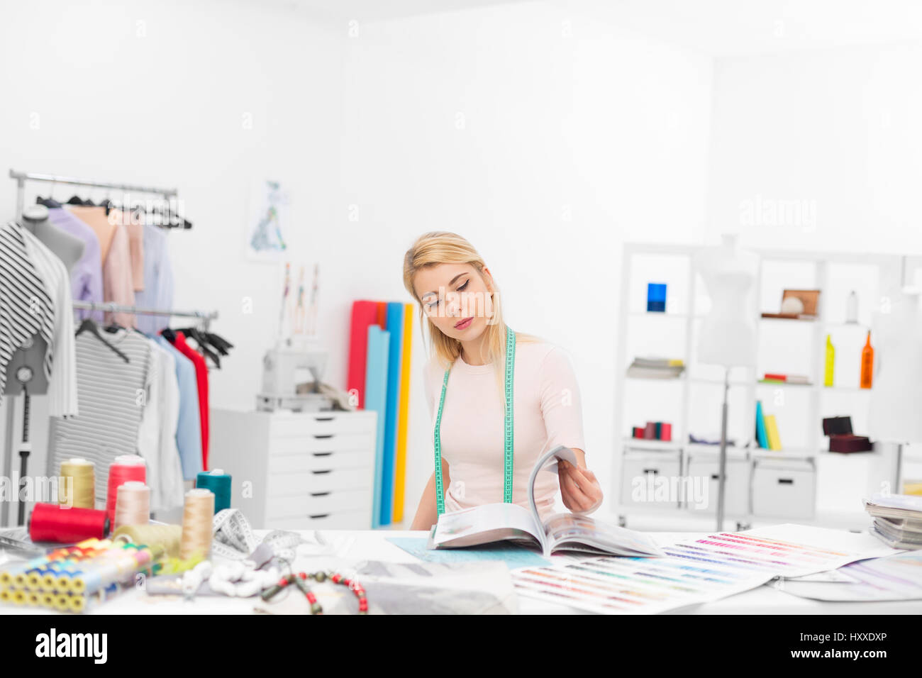 young fashion designer sitting at the desk in her workshop looking throught magazines Stock Photo