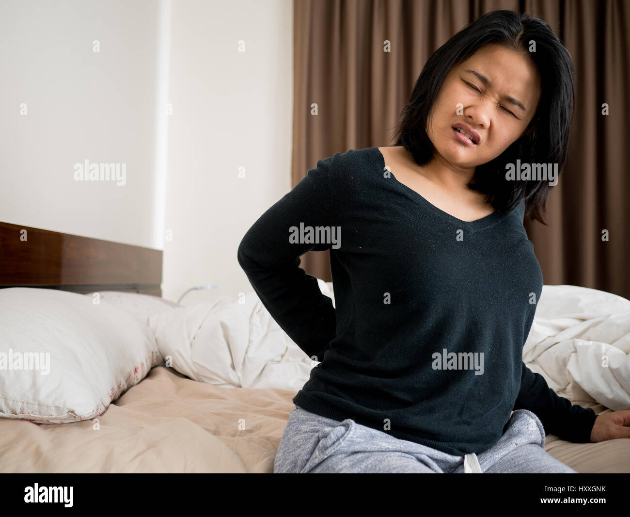 asian woman suffering from back pain sitting on bed Stock Photo